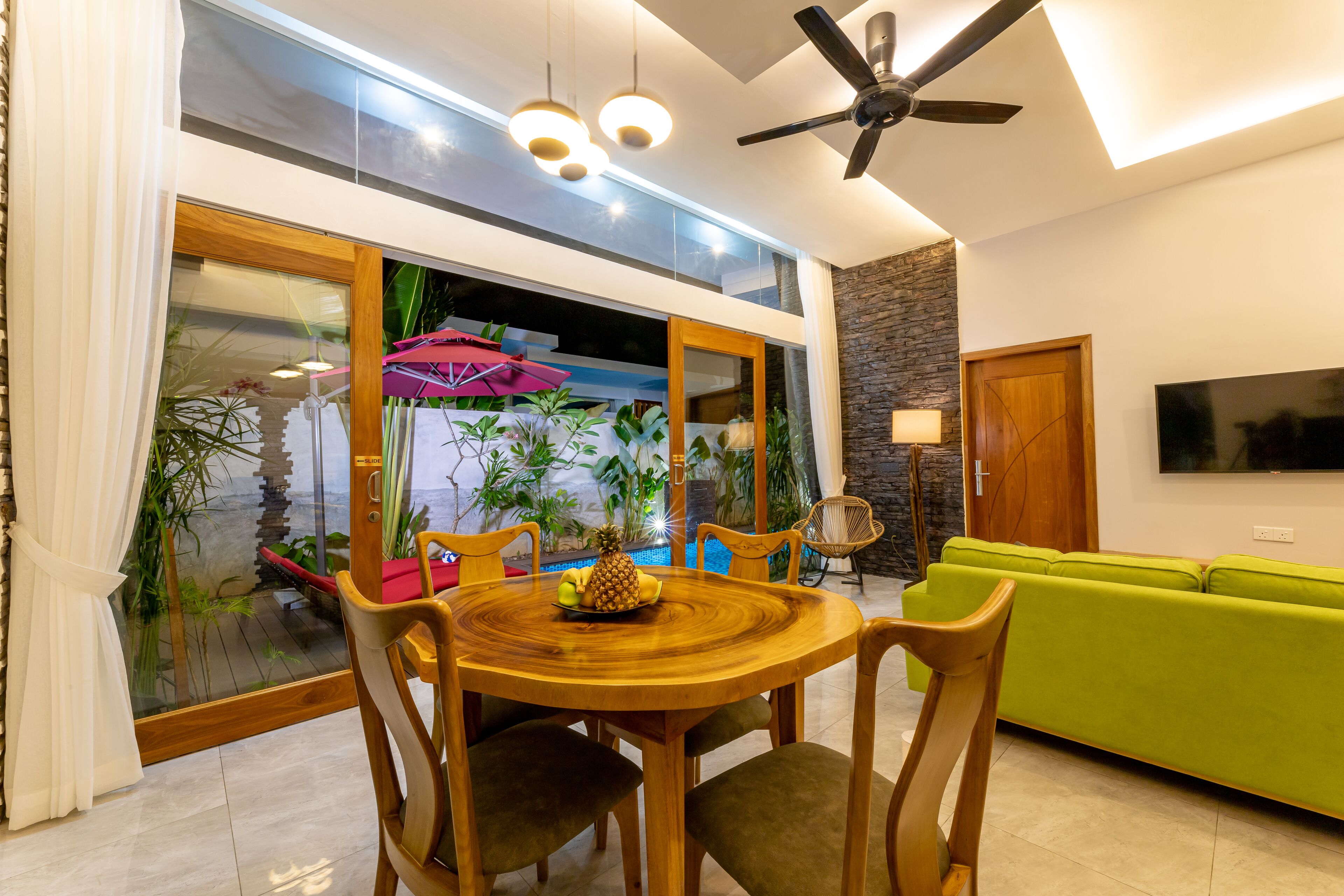 A dining area with a wooden table and chairs, a green sofa, and a TV on the wall.
