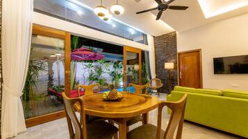 A dining area with a wooden table and chairs, a green sofa, and a TV on the wall.
