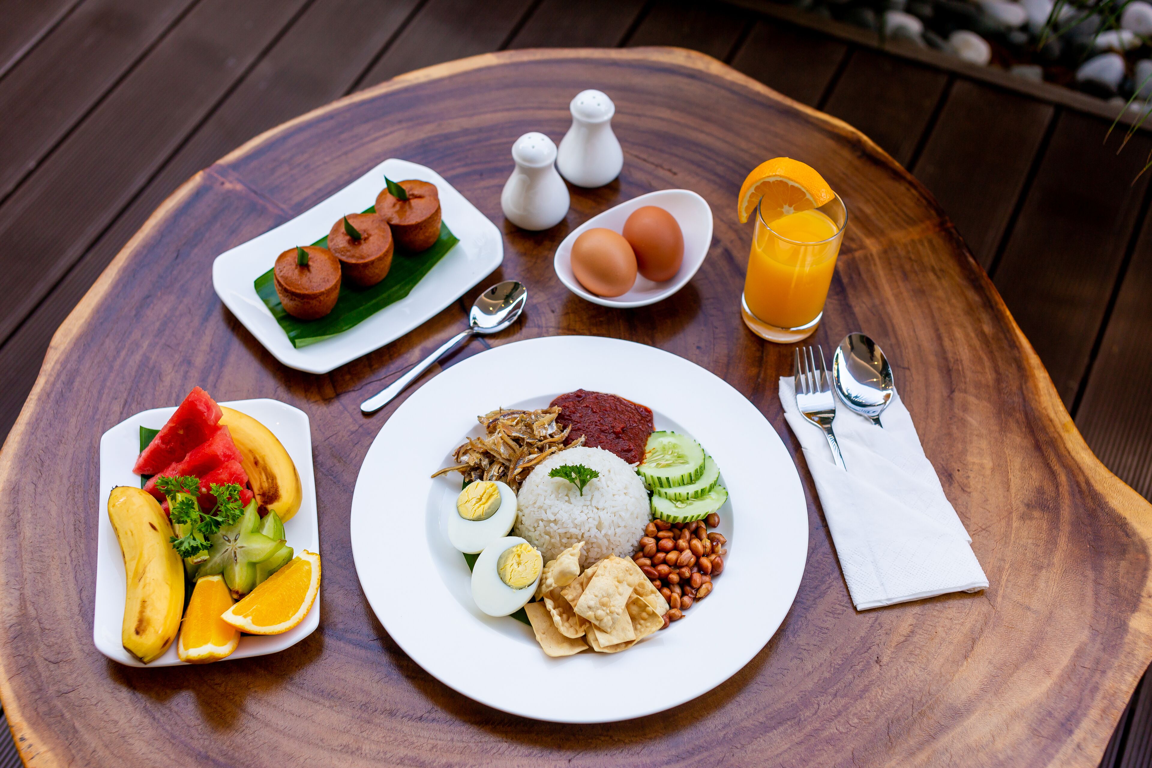 A wooden table with a plate of food, including rice, eggs, and vegetables, and a glass of orange juice.
