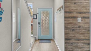 Un couloir avec une porte bleu clair, un mur en bois et un miroir qui reflète le couloir.