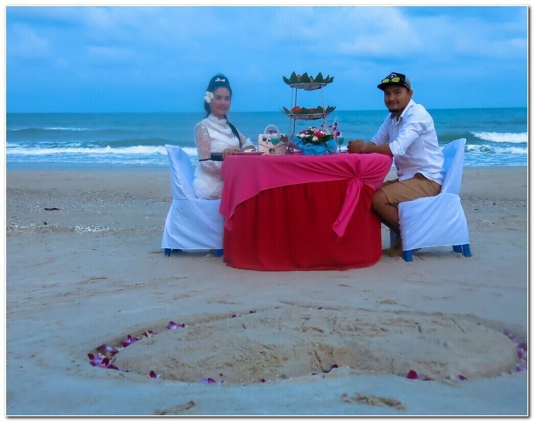 A beachside table with a pink tablecloth, two white chairs, and a decorative centerpiece.