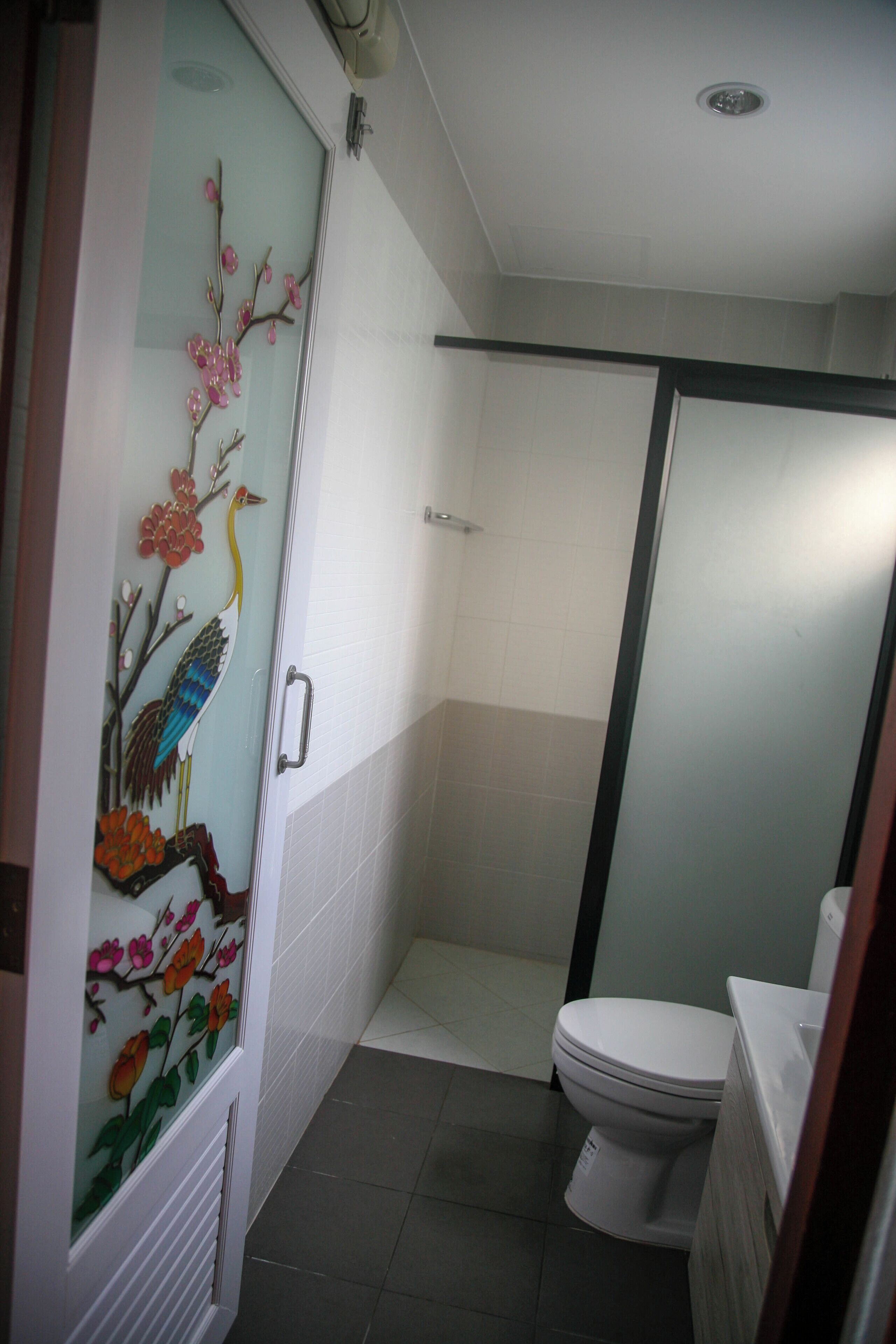 Un baño con inodoro, cabina de ducha y puerta de vidrio decorativa con motivos de pájaros y flores.