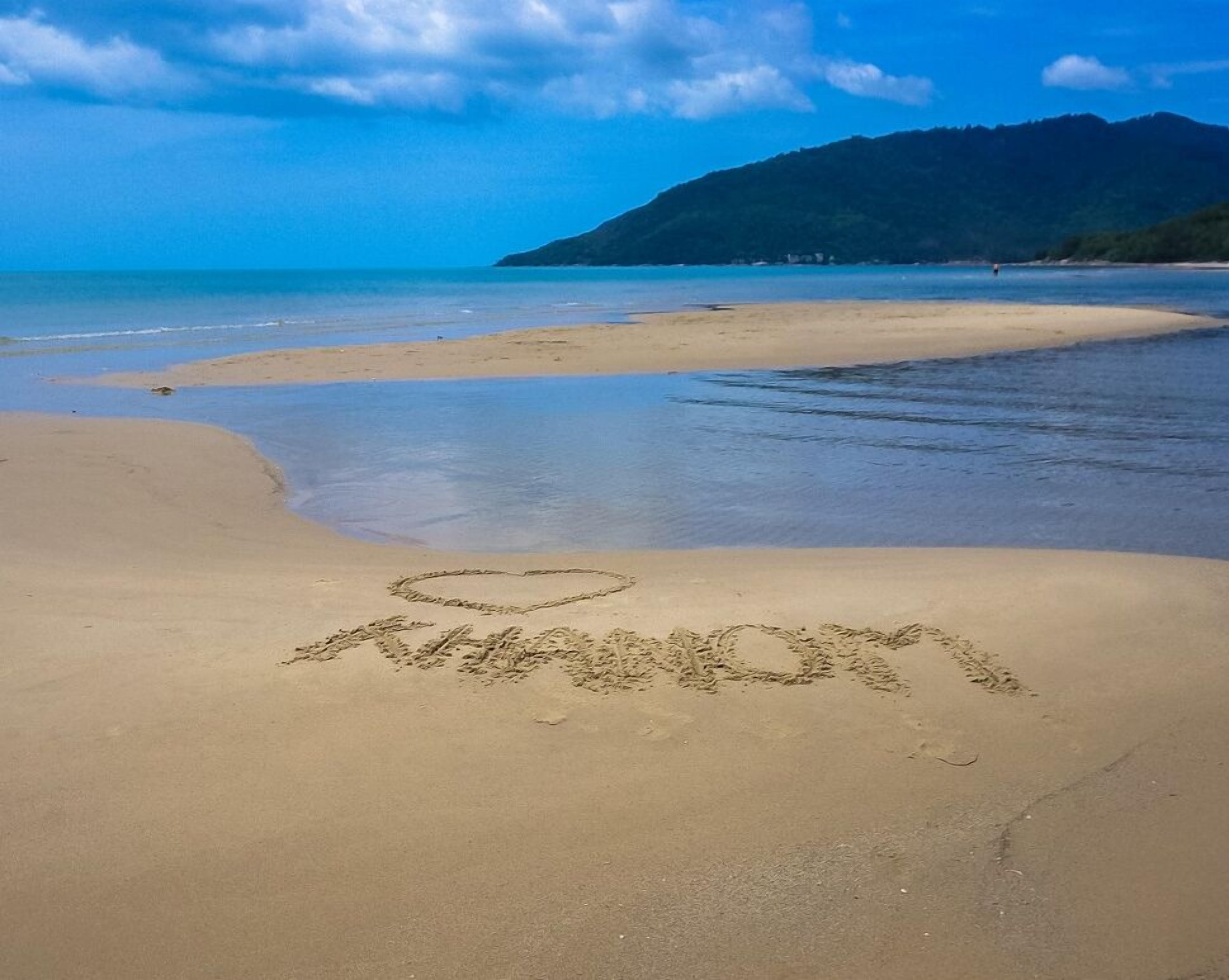 A beach with a heart-shaped word "LOVE" and a heart symbol drawn in the sand.