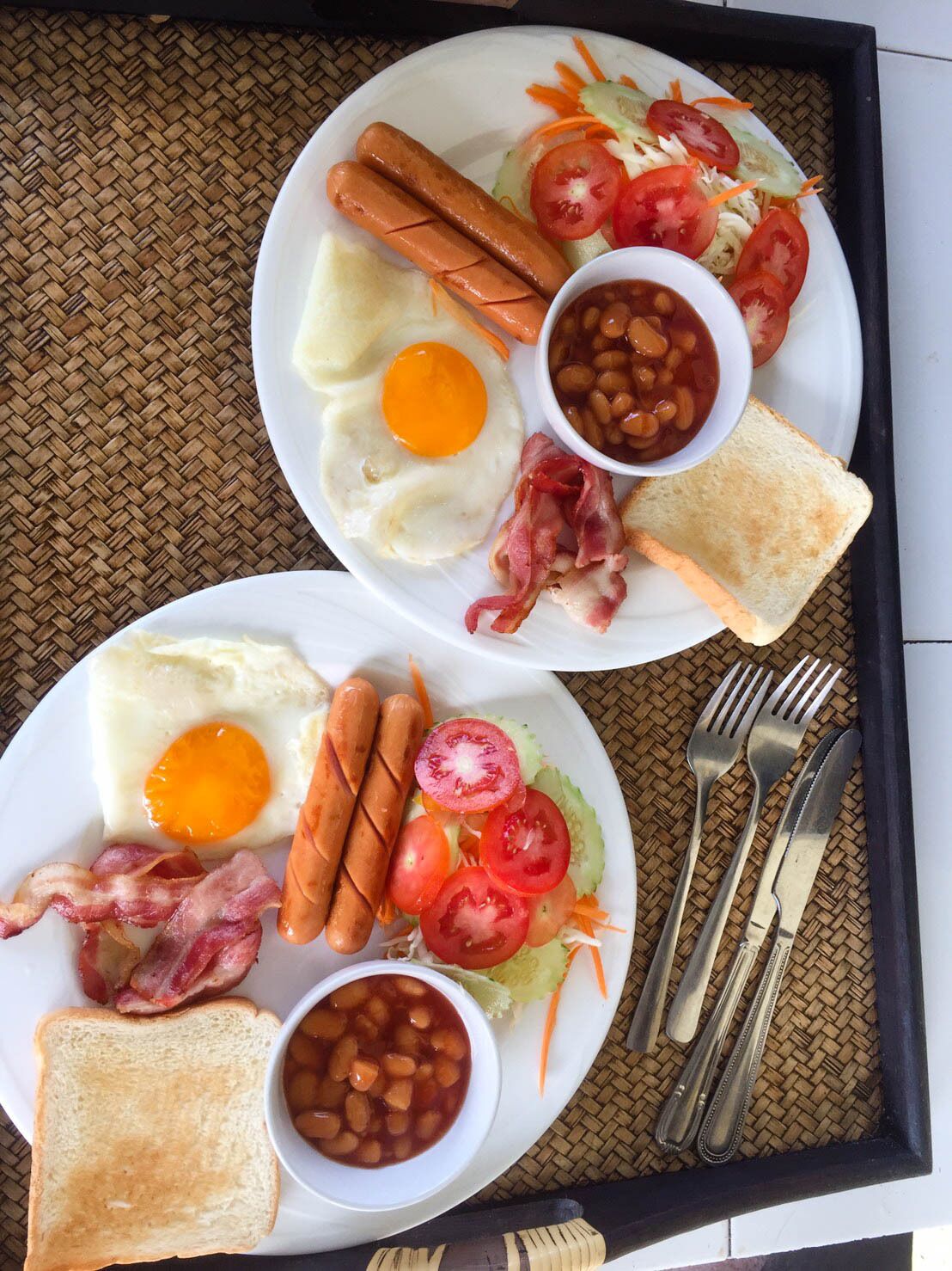 Deux assiettes de nourriture pour le petit-déjeuner, comprenant des œufs, des saucisses, du bacon, des toasts et des haricots.
