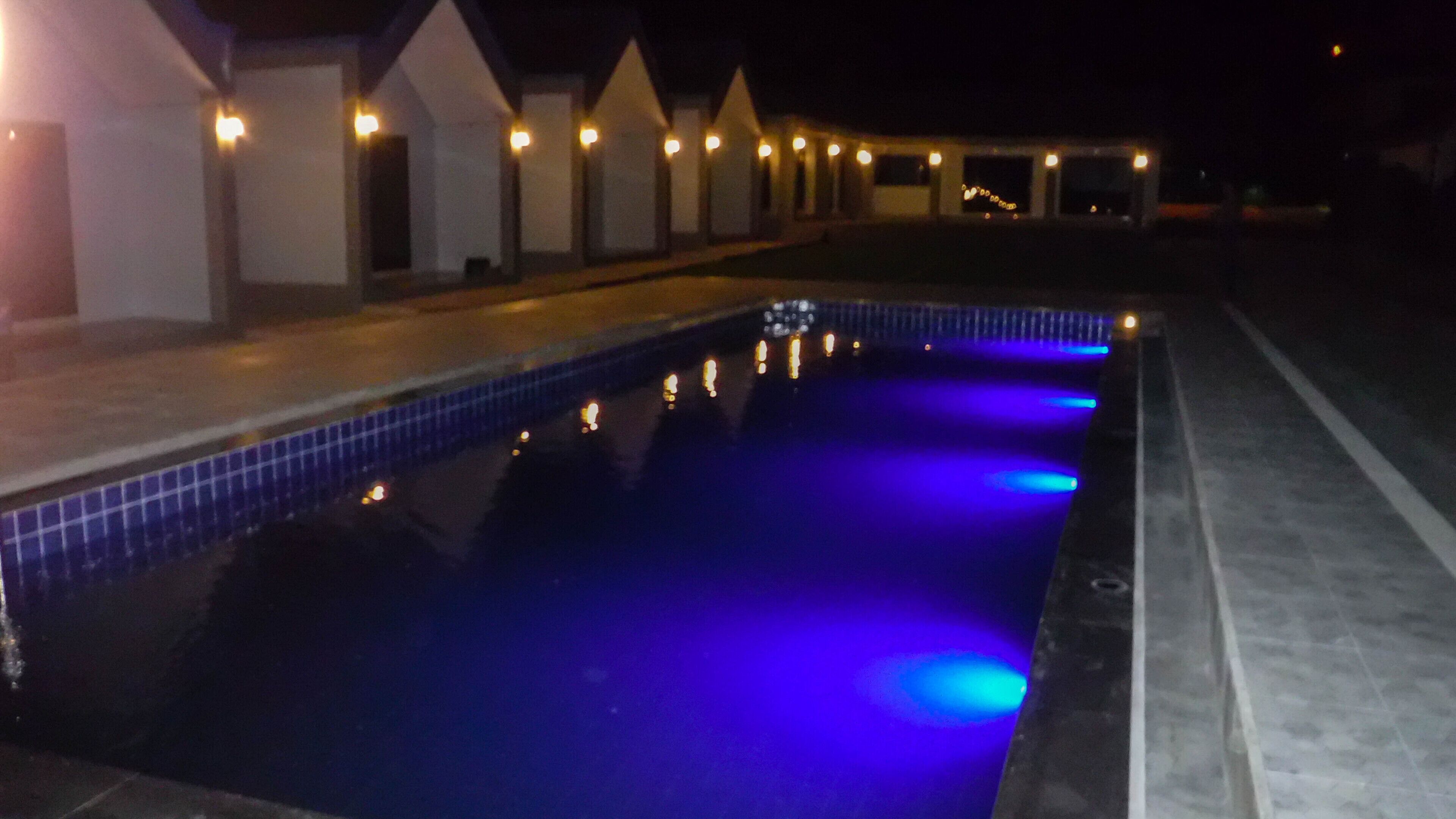 A swimming pool with blue lighting at night, surrounded by a row of buildings with lights on.