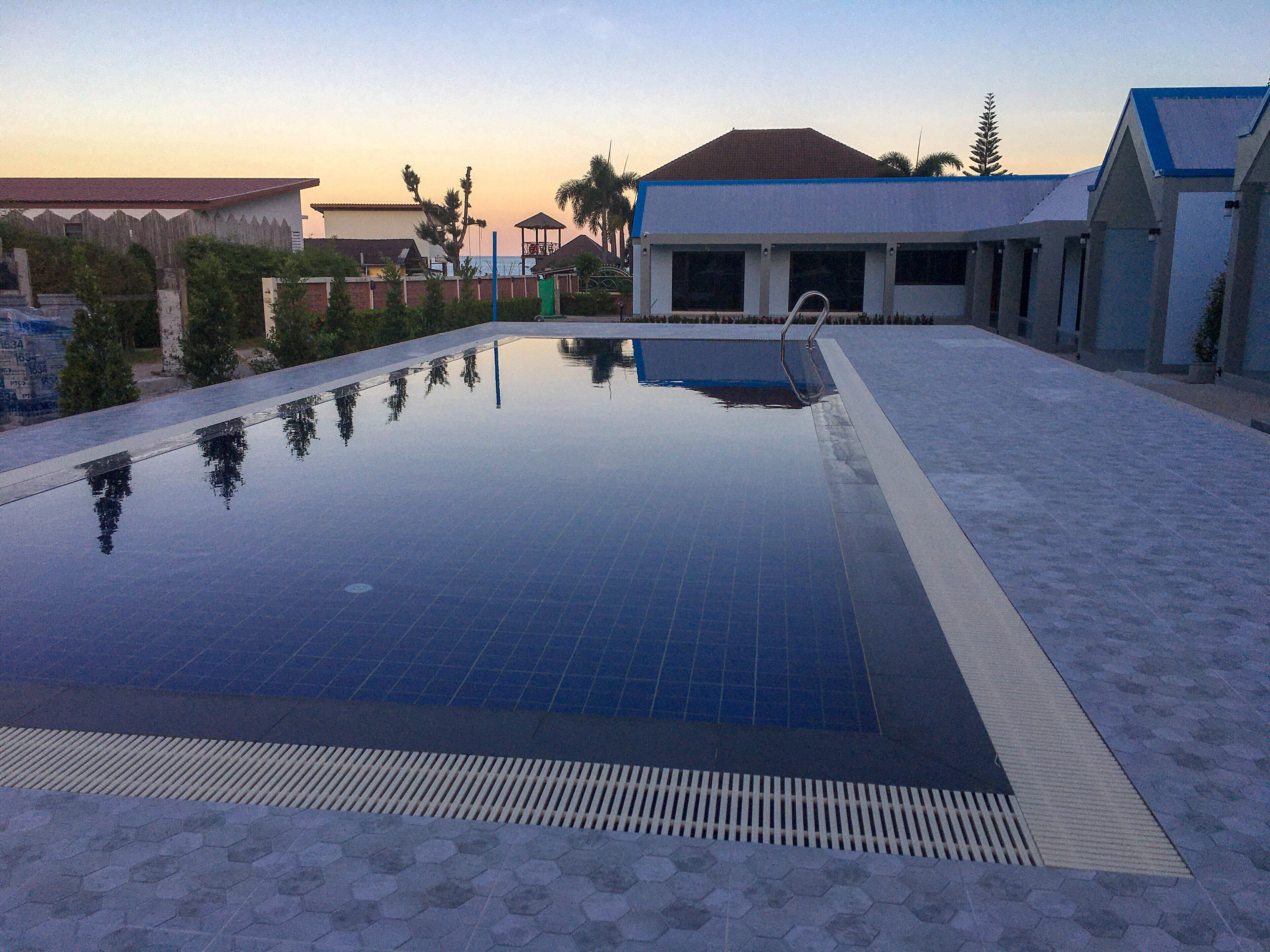 Uma piscina com um deck ladrilhado, cercada por edifícios e palmeiras.