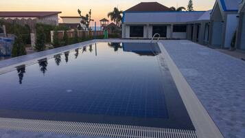 Una piscina con borde de baldosas, rodeada de edificios y palmeras.
