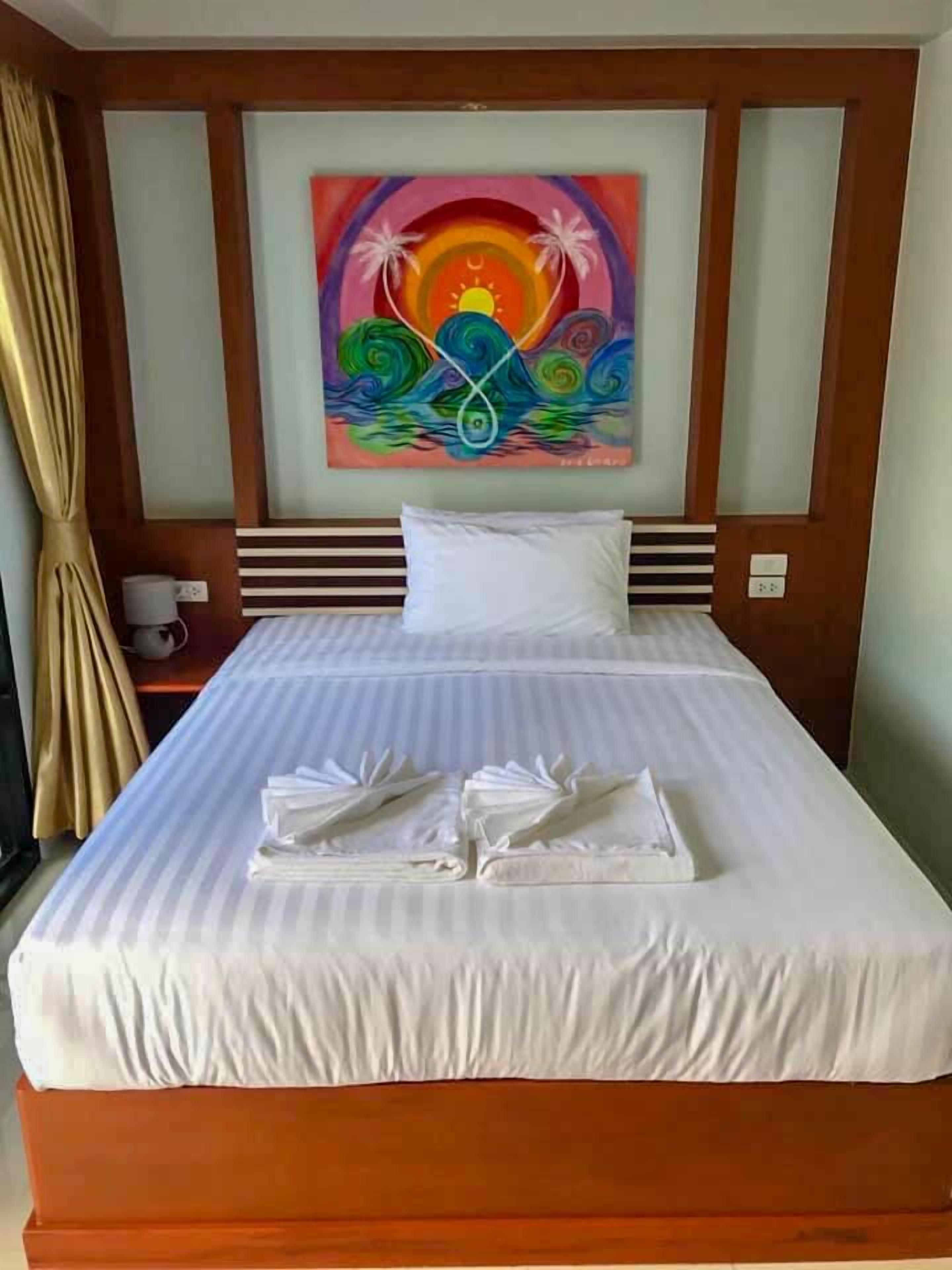 A neatly made bed with white linens and towels, a colorful abstract painting on the wall, and a wooden headboard.