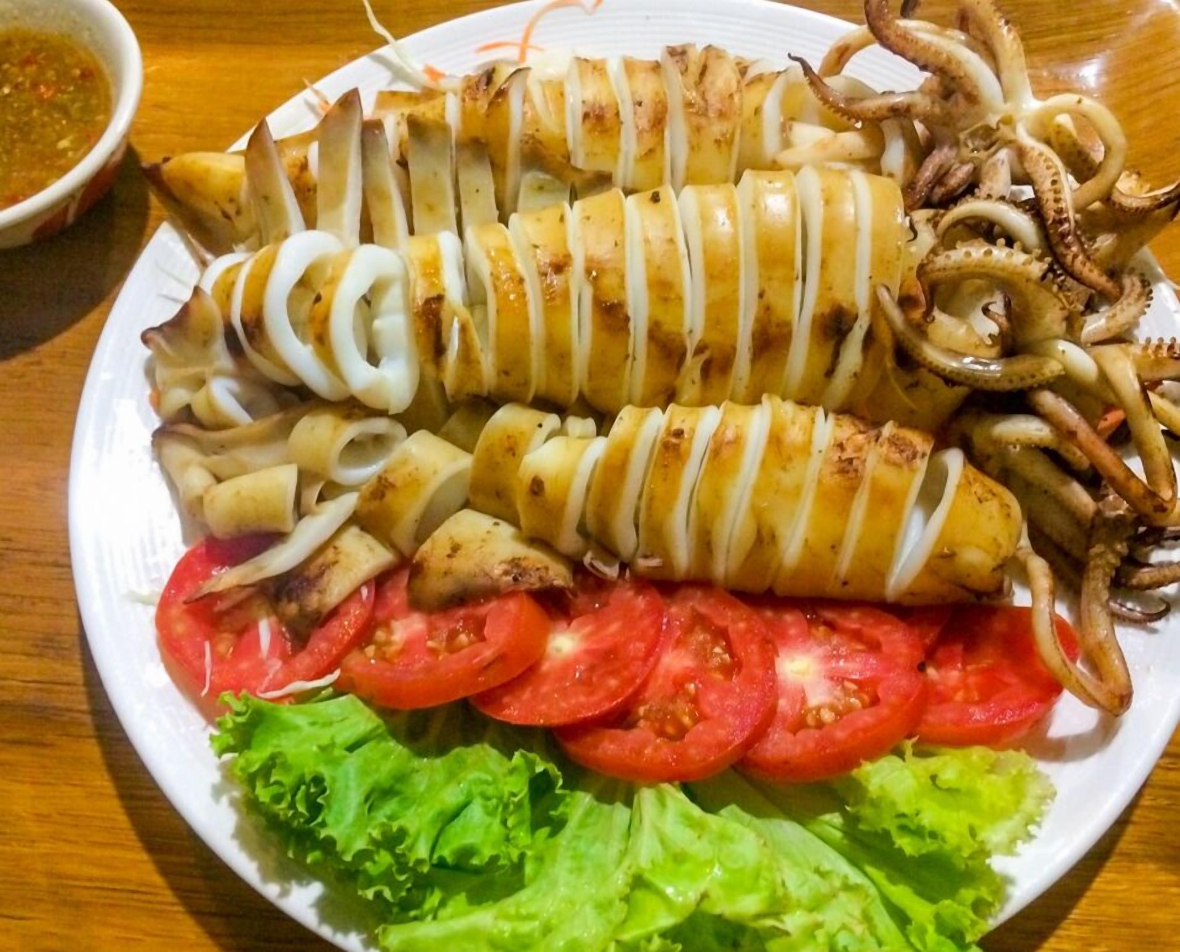 En tallerken med grillet blæksprutte og blød blækspratte, tomatstykker og salat.