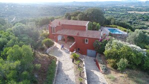 A red villa with a tiled roof, a swimming pool, and a stone pathway leading to the entrance. - 3 bedroom villa with swimming pool in a natural setting  (Arzachena SARDAIGNE)