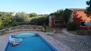 A swimming pool with stone tiles, a stone wall, and a red building with a tiled roof. - 3 bedroom villa with swimming pool in a natural setting  (Arzachena SARDAIGNE)