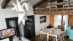 A modern living room with a grey sofa, a dining table with chairs, a TV on the wall, and a star-shaped light fixture. - Chalet Les Angles 1900m (Les Angles)