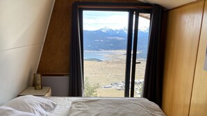 A bedroom with a bed, a bedside table with a lamp, and a window with a view of mountains and a valley. - Chalet Les Angles 1900m (Les Angles)