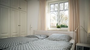Een slaapkamer met een groot bed, twee nachtkastjes, een raam met gordijnen en een kledingkast.