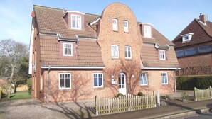 Een tweelaags bakstenen huis met een schuin dak, meerdere ramen en een houten hek voor.