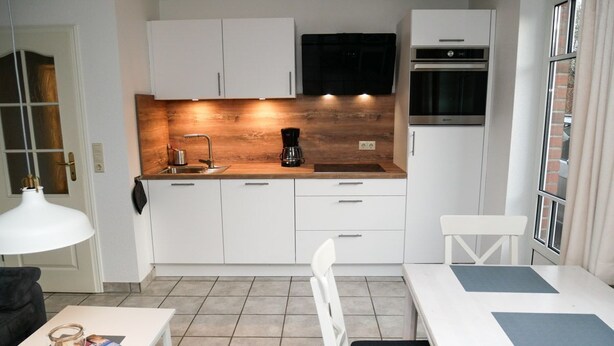 Een kleine keuken met witte kastjes, een inbouwoven en een koffiezetapparaat.