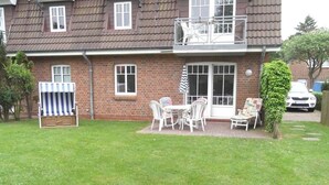 Een bakstenen huis met een balkon, een kleine tuin en een terras met tuinmeubilair.