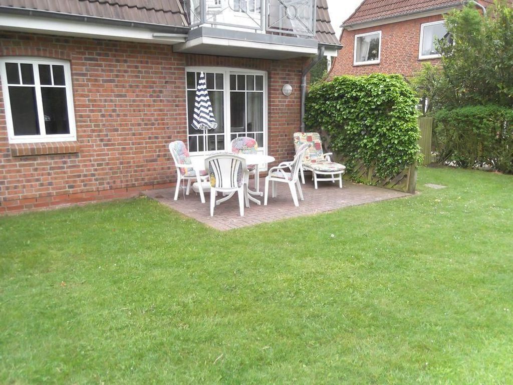 A brick house with a patio area featuring white outdoor furniture and a small table.