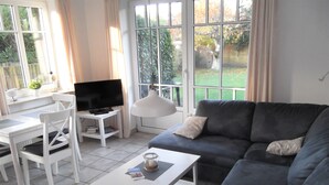 Een woonkamer met een grijze bank, een witte salontafel en een televisie op een witte dressoir.