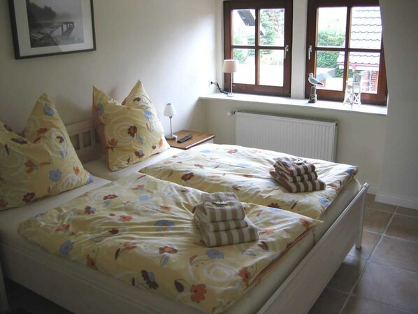 Uma cama de casal com roupa de cama florida, uma mesa de cabeceira com abajur e uma janela com vista para o verde.