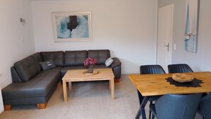 Ett modernt vardagsrum med en hörnsoffa, ett soffbord i trä och ett matbord med stolar.