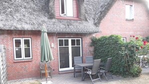 A brick house with a thatched roof, a patio with a table and chairs, and a green umbrella. - Boowen Taarep 19, Germany (Utersum)