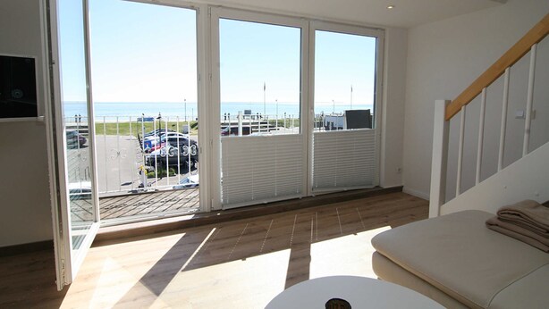 A room with large windows, a wooden floor, a white sofa, and a view of the sea. - Am Wasser OG, Germany (Hörnum (Sylt))