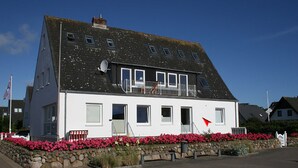 A two-story house with a balcony, a stone wall with flowers, and a flag. - Am Wasser OG, Germany (Hörnum (Sylt))