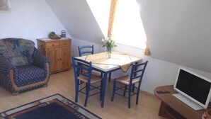 A cozy room with a dining table, chairs, a sofa, a TV, and a window with curtains.
