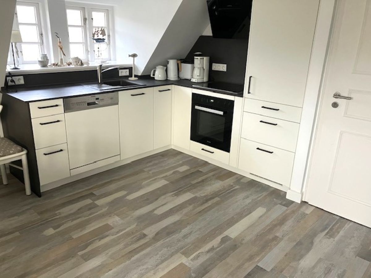 A modern kitchen with white cabinets, a black oven, and a grey herringbone floor.