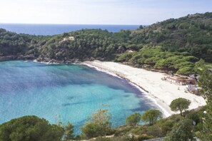 Paesaggio costiero con spiaggia, acque blu cristalline e vegetazione lussureggiante.