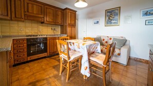 A kitchen with wooden cabinets, a dining table with chairs, and a refrigerator. - Le Isole with large terrace overlooking the sea (Campo nell'Elba)