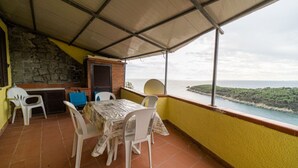A covered terrace with a table and chairs, a stone wall, and a view of the sea. - Le Isole with large terrace overlooking the sea (Campo nell'Elba)