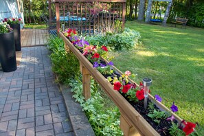 Een tuin met verhoogde bloembedden, een houten pergola en een geplaveid pad.