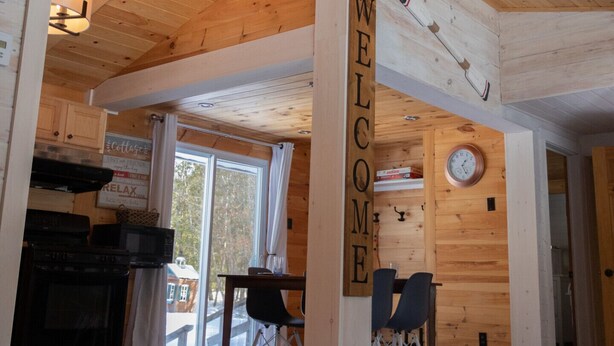 En interiör med träpanel, en takfläkt, en välkomstskylt, en klocka och en matplats med stolar och ett bord.