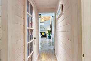 A hallway with wooden walls and a door leading to a living area with a sofa, a table, and a potted plant. - Sandy's Tiki Hut on Sunset Trail Family Beach Retreat-Steps to Beach (Tiny)