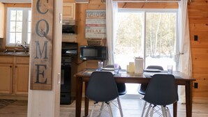 En inredning med träpaneler och en skylt med texten ”VÄLKOMMEN”, ett matbord med stolar, ett köksområde och en utsikt över träd genom fönstret.