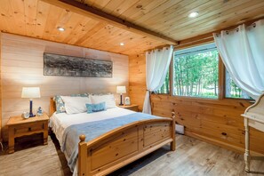 A wooden cabin bedroom with a bed, nightstands, and a window with curtains.