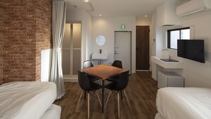 Une chambre d’hôtel avec deux lits, une table à manger en bois avec des chaises, un petit coin cuisine, un téléviseur fixé au mur et un mur décoratif en briques.