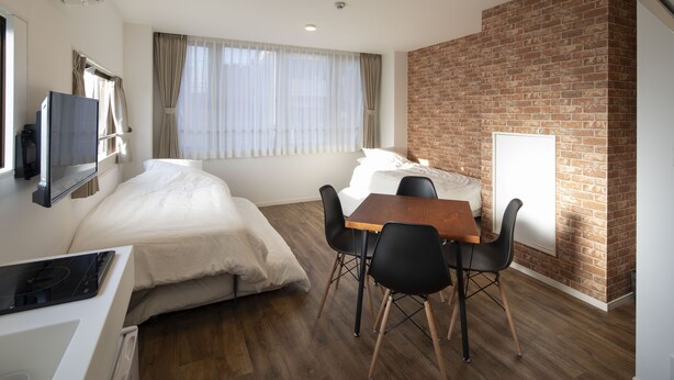 Une chambre d’hôtel de taille réduite, comprenant un lit, une table à manger avec des chaises, un téléviseur et un mur décoratif en briques.