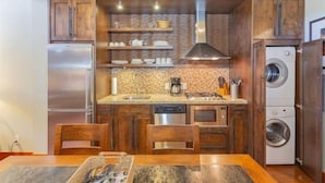 Cocina compacta con armarios de madera, lavavajillas integrado, refrigerador de acero inoxidable, cafetera y lavadora.