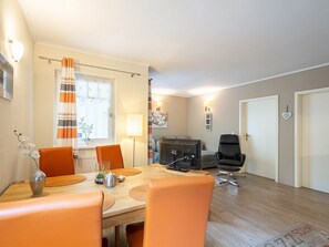 A dining area with a wooden table, orange chairs, a black office chair, and a window with curtains.