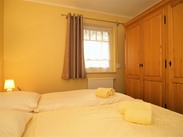 A bedroom with two beds, a window with curtains, a radiator, and wooden wardrobes.