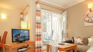 Una sala de estar con televisor, muebles de madera, un sofá, una mesita y vistas al exterior a través de un ventanal.