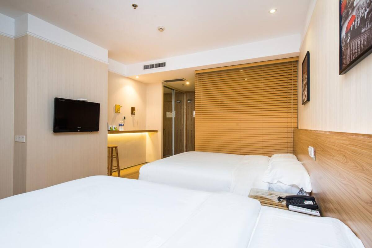 Ein Hotelzimmer mit zwei Betten, einem an der Wand befestigten Fernseher, einem Holz-Kopfteil und einem kleinen Schreibtisch mit Stuhl.