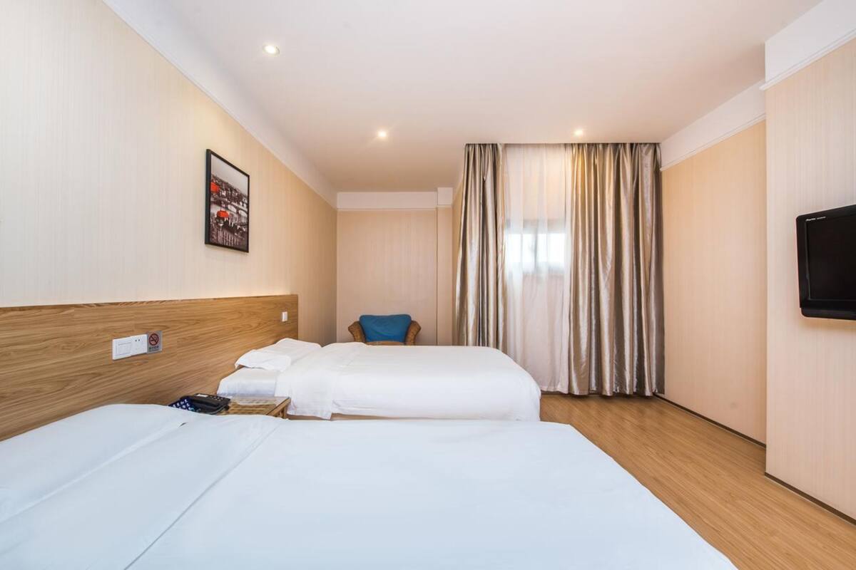 Ein Hotelzimmer mit zwei Betten, einem Sessel, einem Fernseher und einem Fenster mit Vorhängen.