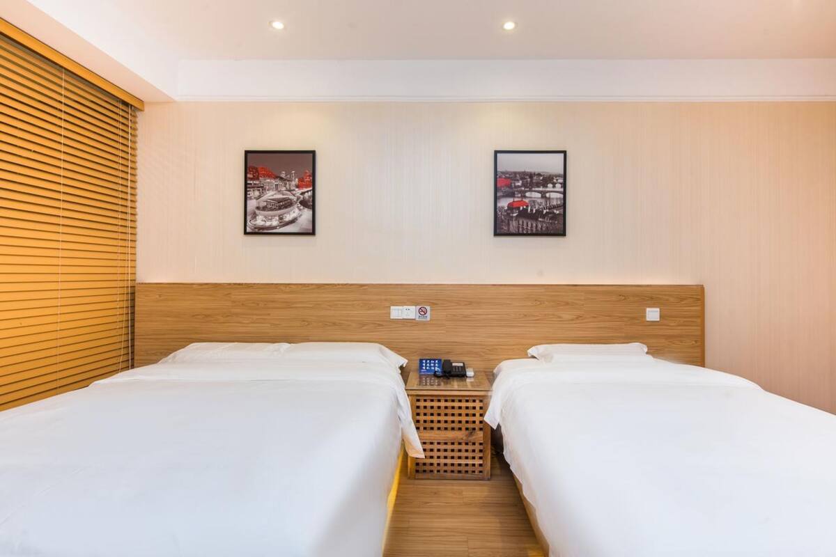 Ein Hotelzimmer mit zwei Einzelbetten, einem hölzernen Kopfteil und zwei gerahmten Bildern an der Wand.