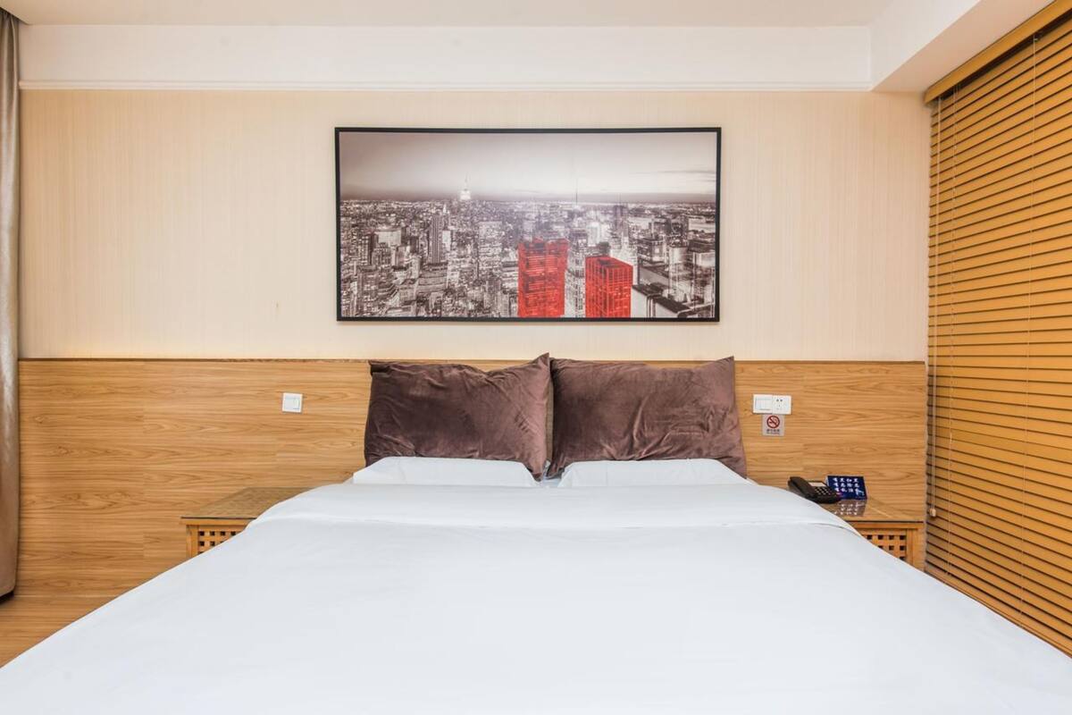 Ein Hotelzimmer mit einem großen Bett, einem Holzkopfteil, einem Stadtbild an der Wand und einem Telefon auf dem Nachttisch.