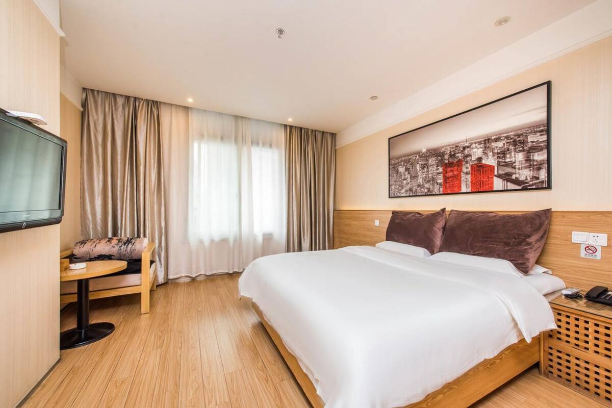 Ein Hotelzimmer mit einem großen Bett, einem Fernseher, einem kleinen Tisch und einem Fenster mit Vorhängen.