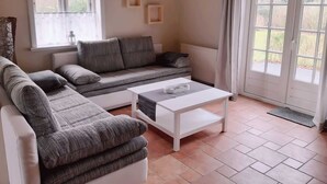 Uma sala de estar acolhedora com um sofá cinzento, uma mesa de centro branca e uma janela com cortinas.